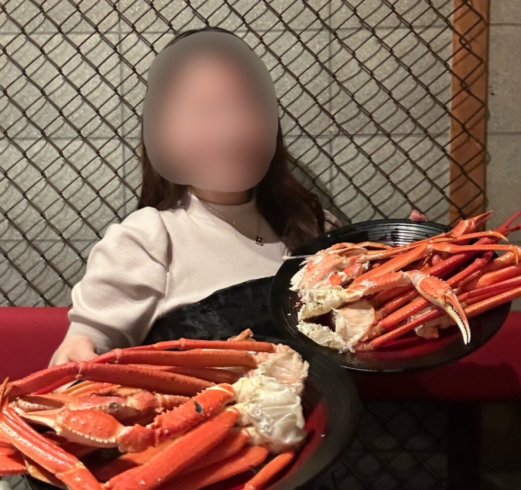 本ズワイガニの皿を両手に持って笑顔の女性。蟹の食べ放題を満喫中の様子(顔はぼかし加工済み)