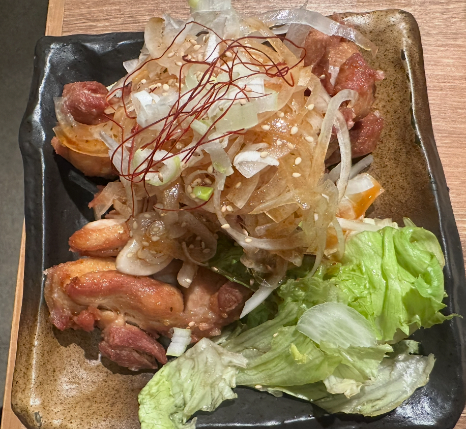 黒い皿に盛り付けられたパリパリに揚げた鶏肉に、たっぷりのスライス玉ねぎと糸唐辛子がのったパリパリ油淋鶏。横にレタスが添えられている