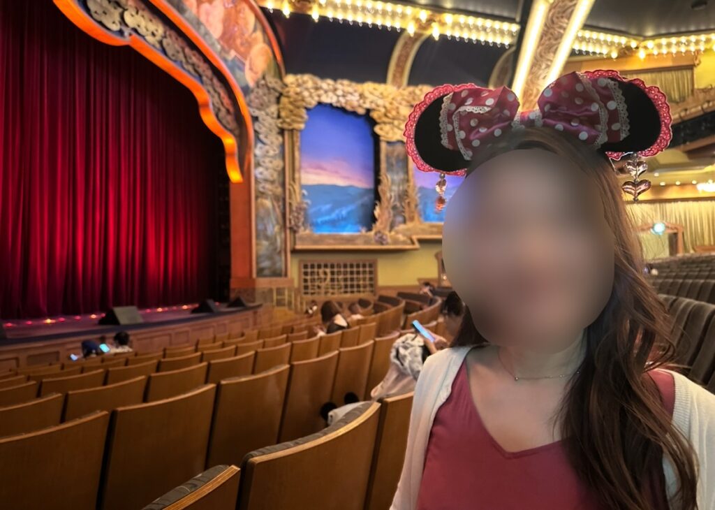 ブロードウェイ・ミュージックシアター内の赤いカーテン前で、ミニーのカチューシャをつけた女性が観劇を待つ様子。