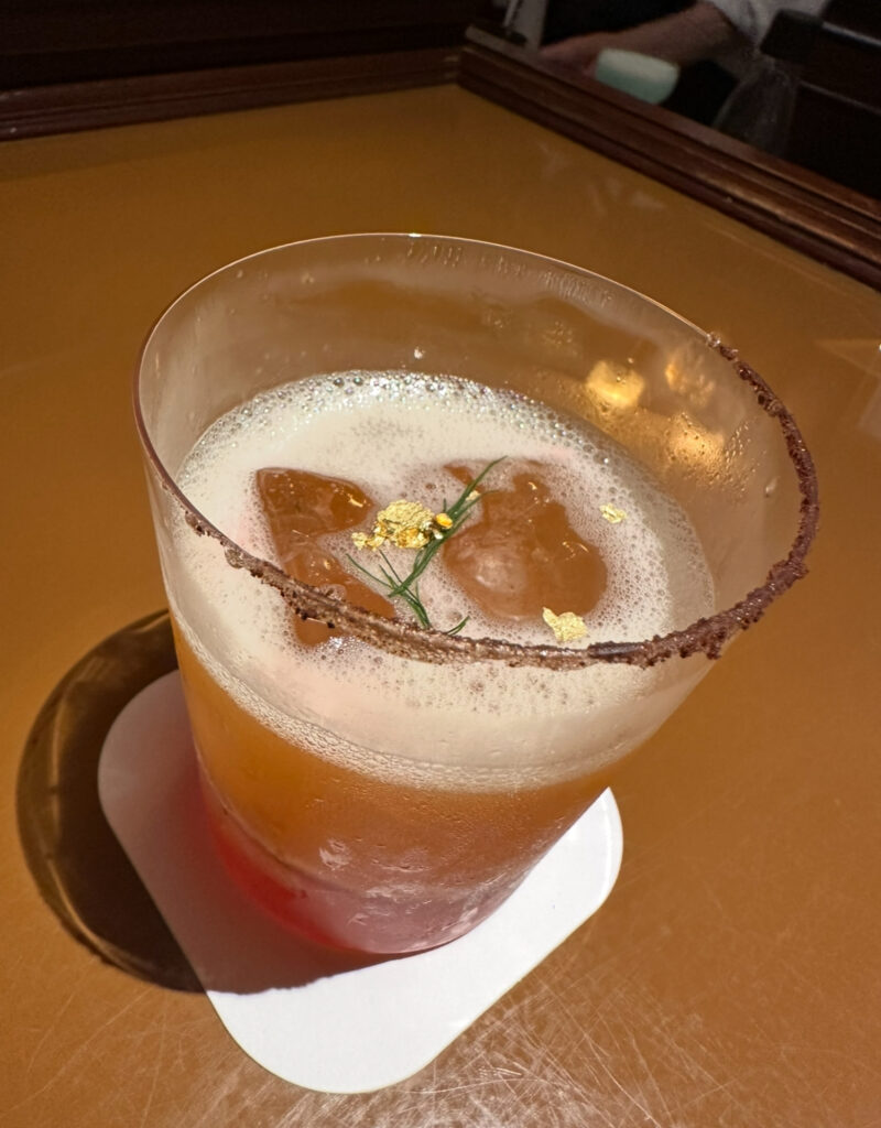 金箔とハーブがトッピングされた、泡立ちのあるおしゃれなカクテル、ギフト・フロム・テディ。