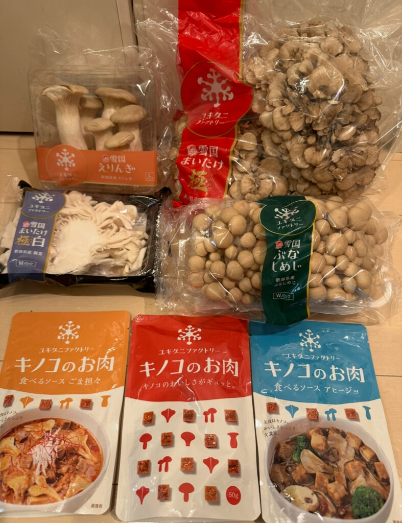 ユキグニファクトリーの株主優待で届いた全体セット。雪国えりんぎ、舞茸極、舞茸極白、ぶなしめじWパックの生鮮きのこ4種類と、「キノコのお肉」シリーズ3種（ごま担々、アヒージョ、しょうがギュッと）が並べられている。