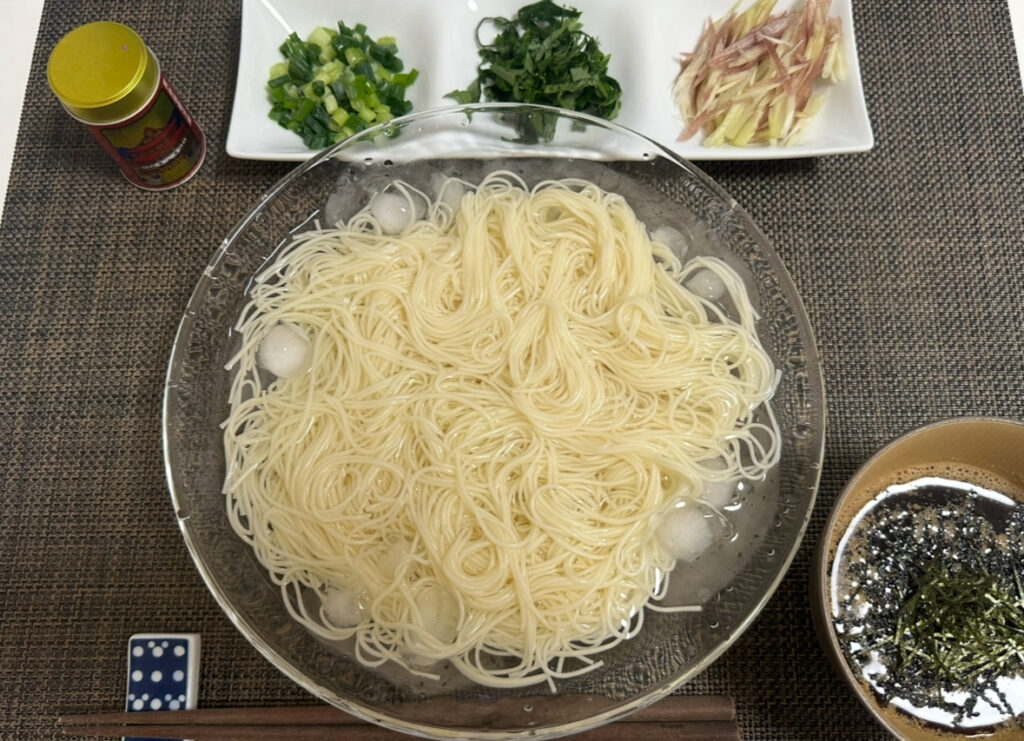 ドウシシャ株主優待の島原手延べそうめんを氷水で冷やし、つけだれと薬味付きでいただいた実食の様子。ネギやみょうが、大葉などの薬味が並び、夏にぴったりの涼しげな食卓。