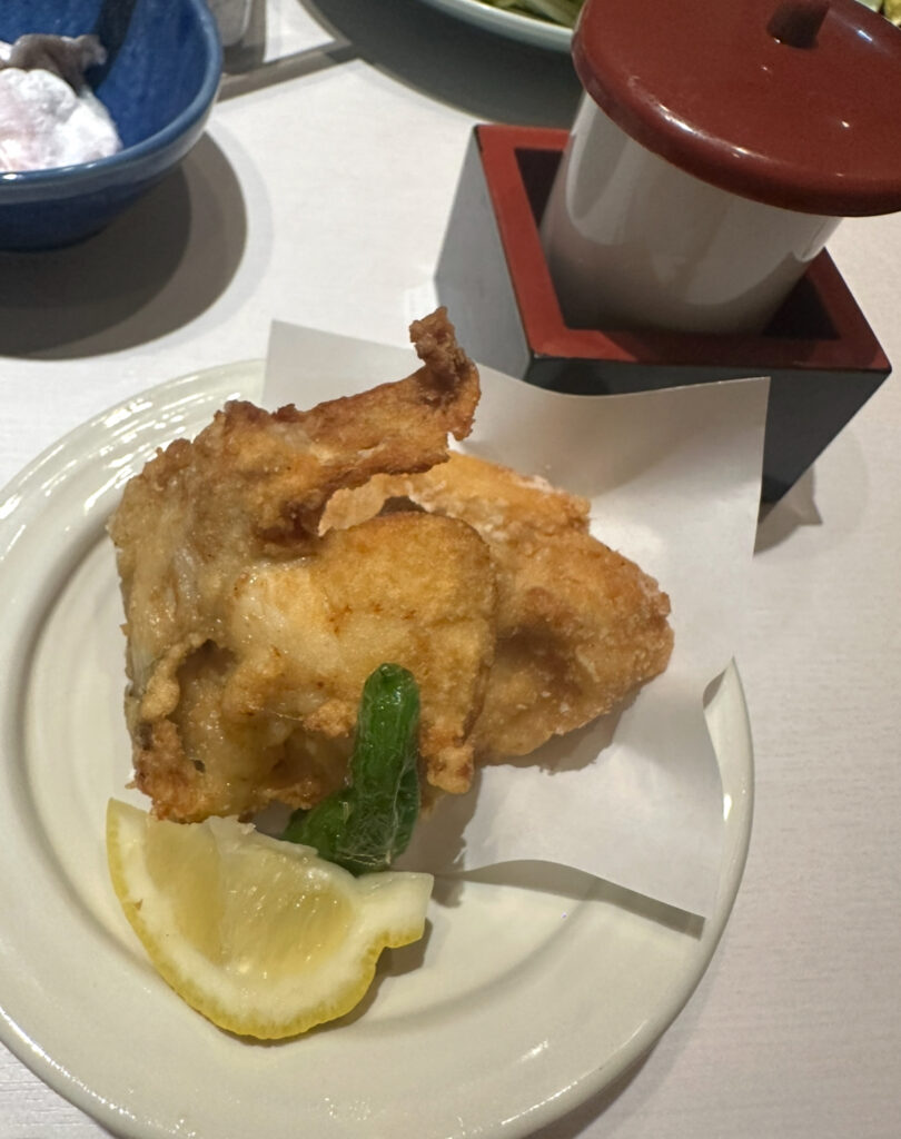 白い皿に盛られたふぐの唐揚げ。衣がカラッと揚がり、レモンとししとうが添えられている。