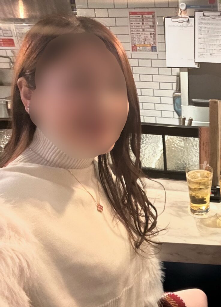 カウンター席でハイボールを楽しむブログ運営者COCOの様子。白のタートルニットとピンクのネックレスが上品な雰囲気を演出している。※顔はぼかしを入れて掲載しています。