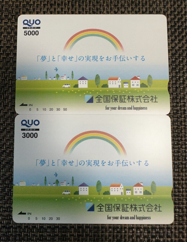 全国保証の株主優待でもらえるQUOカードの写真。上が5,000円分、下が3,000円分で、どちらも虹と家並みが描かれたオリジナルデザイン。