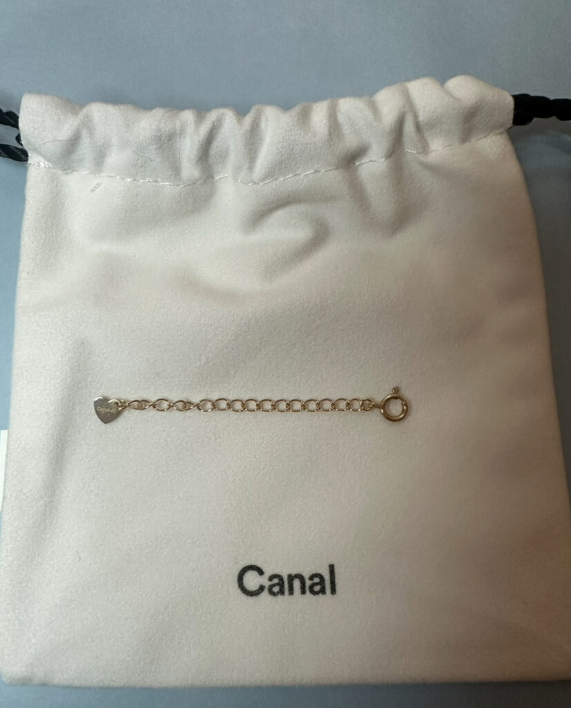 株主優待で入手したCanal 4°Cのアジャスターチェーン。白い巾着袋の上に、ハート型プレート付きのゴールドチェーンが置かれている。