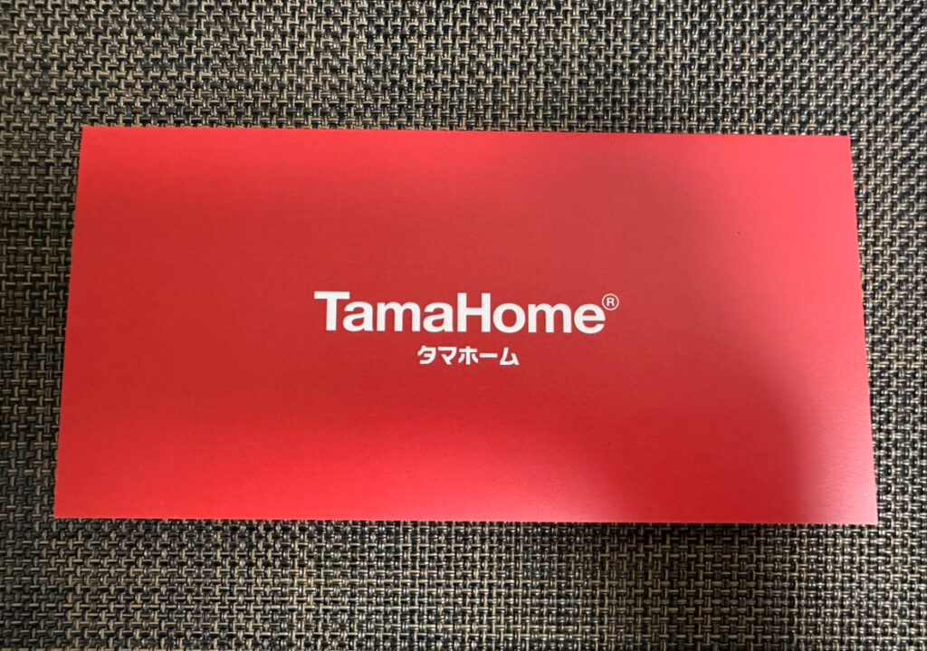 タマホーム株主優待が入った赤い入れ物の表紙。中央に白字で『TamaHome(タマホーム)』と印字されている。
