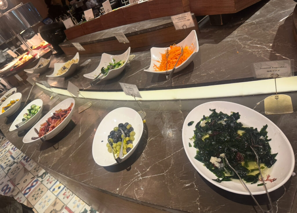 RIO GRANDE GRILL横浜ベイクォーター店のサラダバー前菜コーナー。海藻サラダ、キャロットラペ、オリーブ、パプリカ、ズッキーニ、南瓜など色とりどりの前菜が並んでいる。