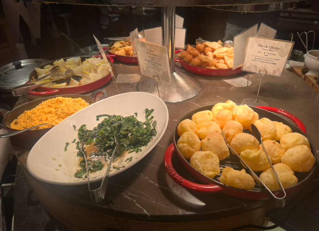 RIO GRANDE GRILL横浜ベイクォーター店のビュッフェ料理。ブラジル定番のチーズパン「ポンデケージョ」、炒めた青菜、ファロッファ、キャッサバなどが色鮮やかに並ぶ。