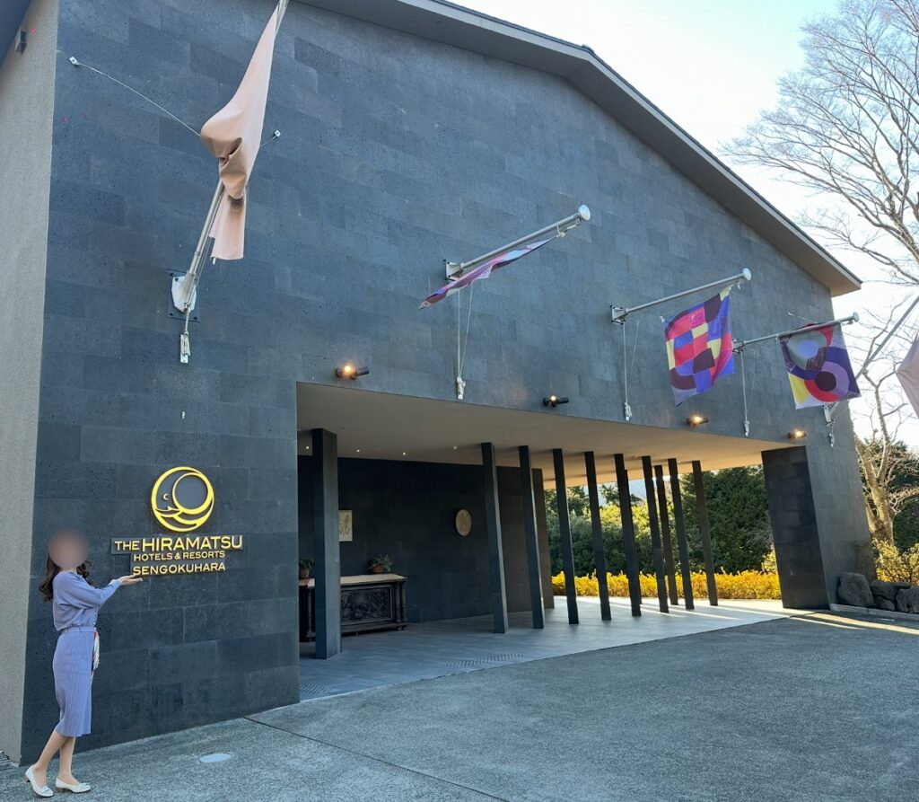 THE HIRAMATSU HOTELS & RESORTS 仙石原のエントランス前で、看板を指差すブログ運営者COCO。優待を使って宿泊した際の記念写真。※顔はぼかしを入れて掲載しています。