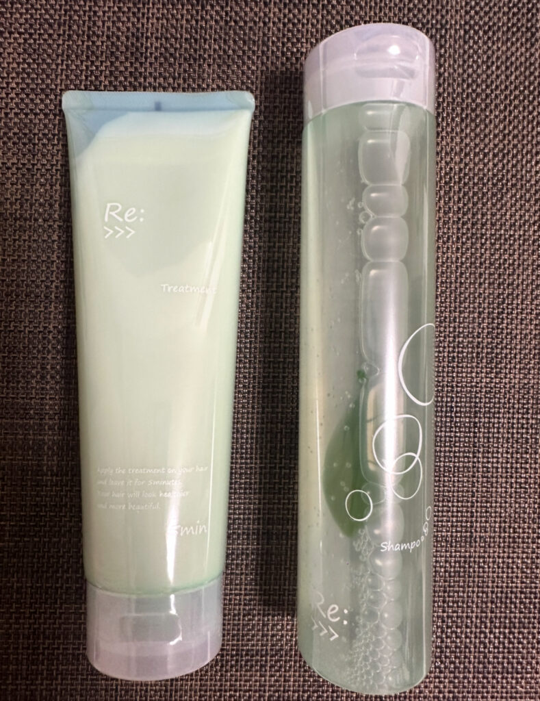 アジュバン株主優待で届いた「Re:>>>」シリーズのシャンプーとトリートメント。美容室専売の高品質ヘアケア製品で、透明ボトルのシャンプーと淡いグリーンのチューブ型トリートメントが並んでいる。