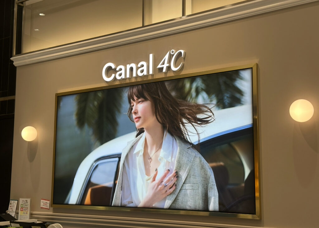 有楽町マルイのCanal 4℃店舗内に設置された大型ビジュアルディスプレイ。モデル女性が白シャツとジャケット姿でアクセサリーを身につけた、洗練されたブランドイメージが印象的。