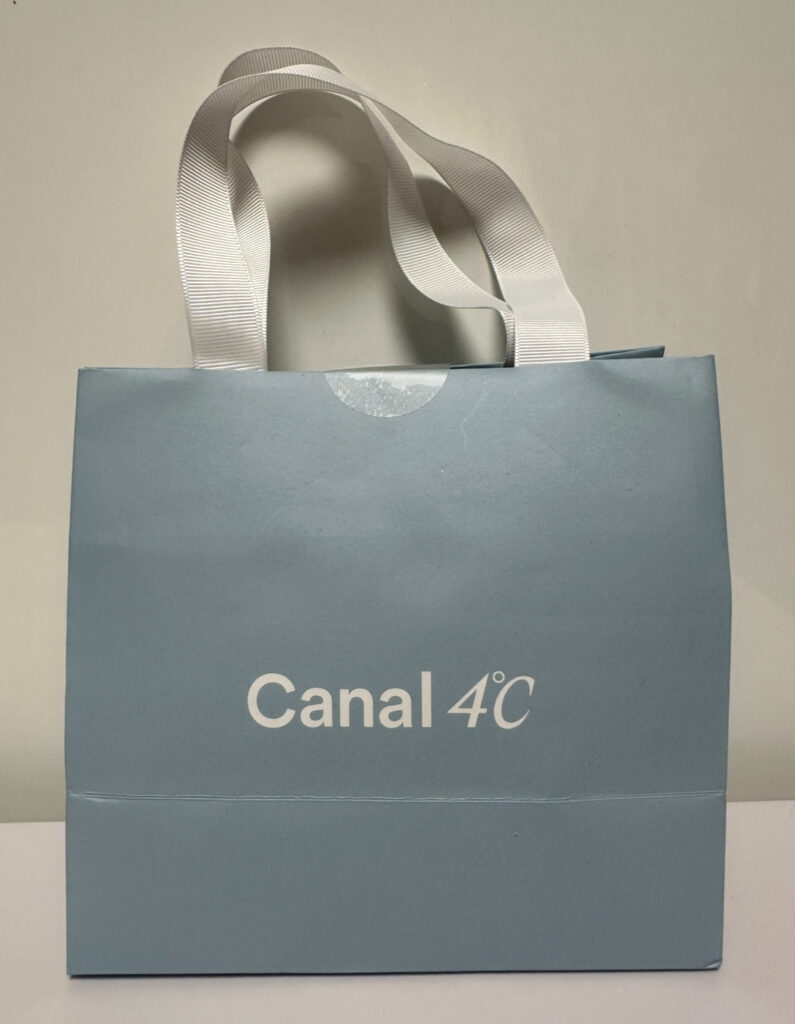 Canal 4℃の淡いブルーの紙袋。白いリボンの持ち手がついた可愛いデザインで、購入したアクセサリーが中に入っている。