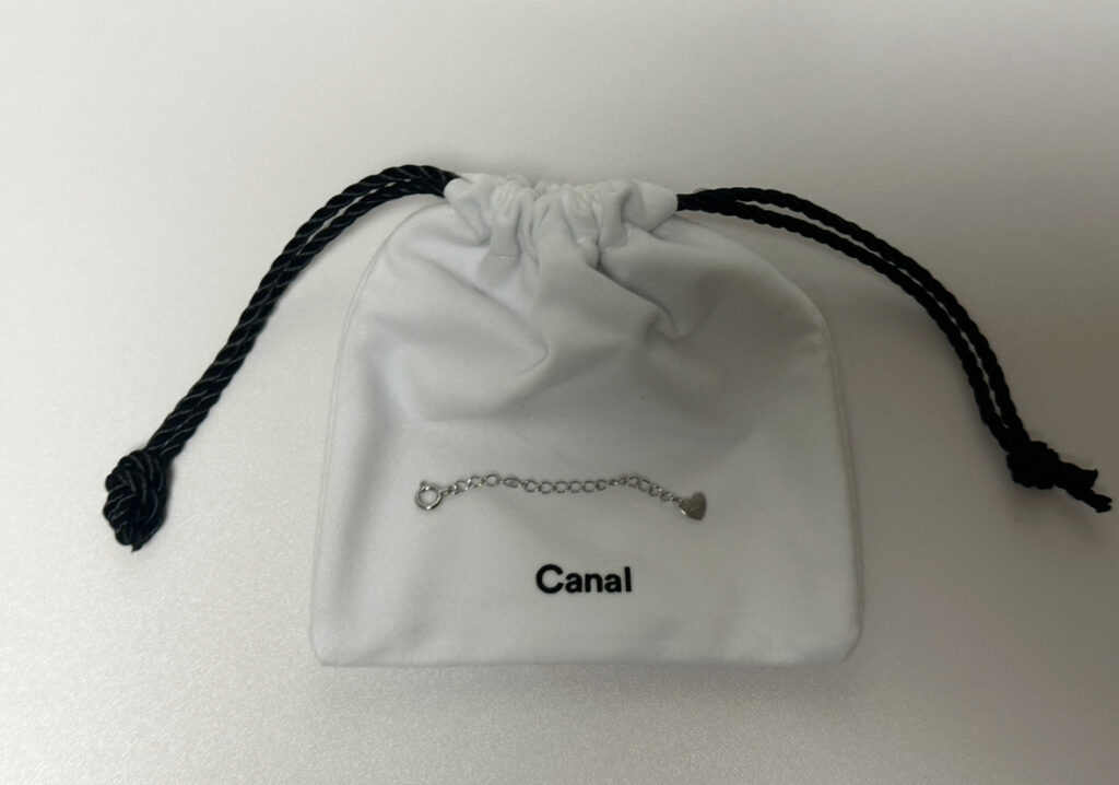 Canal 4℃で購入したK10ホワイトゴールドのアジャスターチェーン。白い巾着ポーチの上に乗せた実物写真で、先端には小さなハートチャームが付いている。