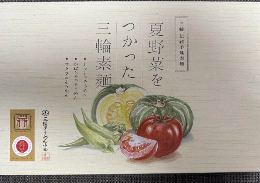 「エスリードの株主優待で届いた『夏野菜を使った三輪素麺』の外箱。木目調の上品なパッケージに、トマト・かぼちゃ・オクラのイラストと『三輪素麺』『夏野菜をつかった三輪素麺』の文字が印刷されている。」