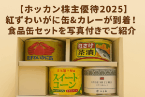 ホッカンホールディングスの株主優待2025を紹介するブログ記事のアイキャッチ画像。紅ずわいがに缶、紅さけ茶漬け缶、スイートコーン缶、五島軒のイギリス風カレー缶の詰め合わせが箱にきれいに並んでいる様子を上から撮影した写真風デザイン。