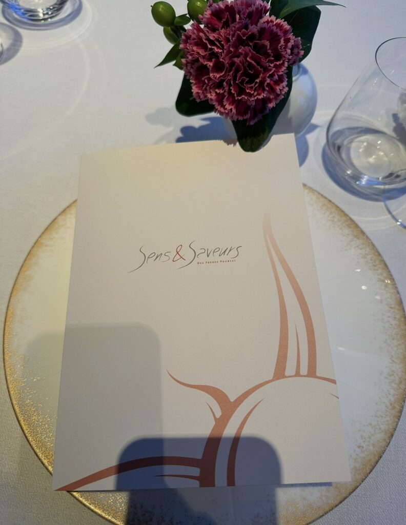 丸の内ビル35階「サンス・エ・サヴール」のディナー席に用意されたコースメニューと花のテーブルセッティング。上品で華やかな雰囲気。