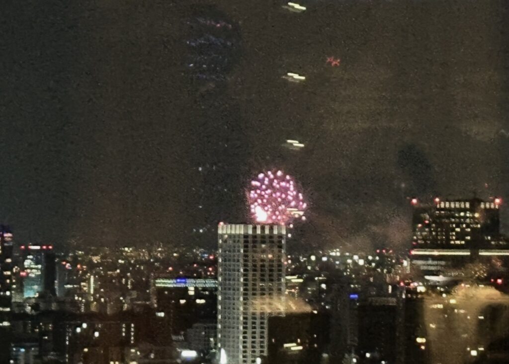 丸ビル35階「サンス・エ・サヴール」から見えた神宮外苑花火大会の様子。夜景の向こうに花火が咲く幻想的な景色。