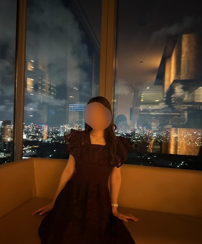 サンス・エ・サヴールの窓際席で夜景を背景にくつろぐブログ運営者COCO。※顔はぼかしを入れて掲載しています。