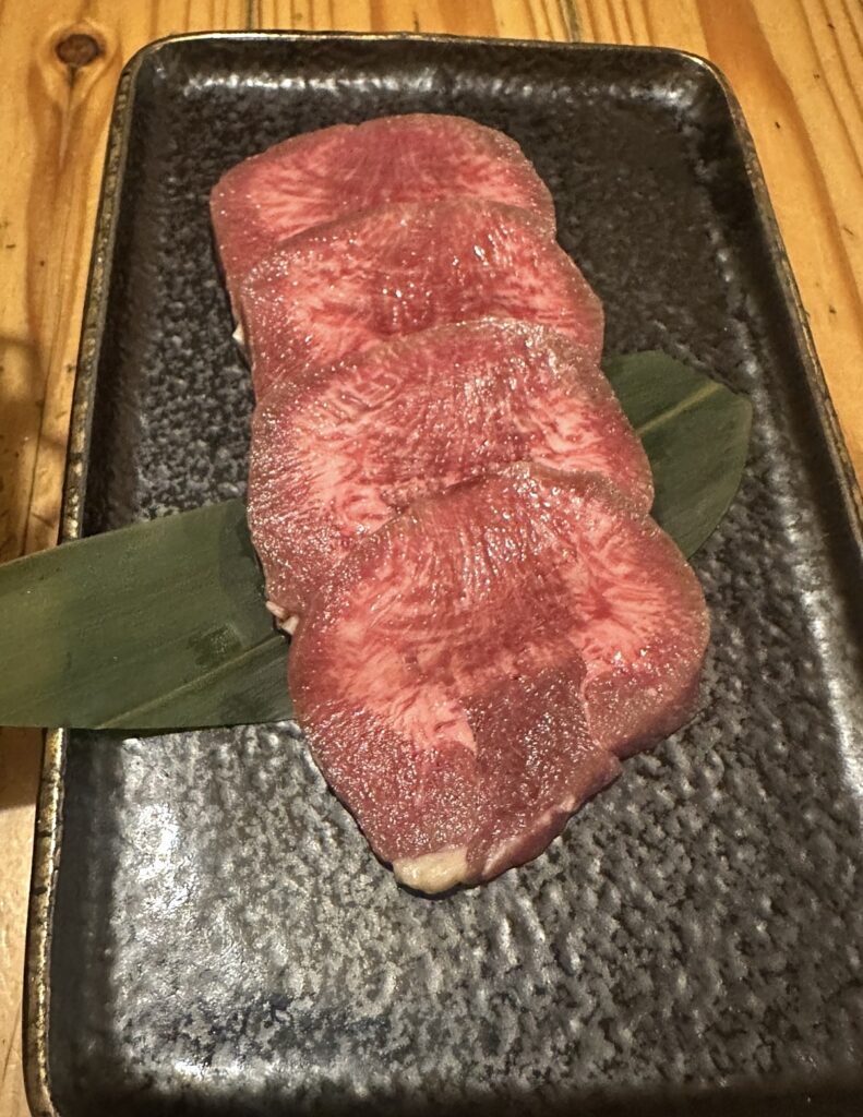 牛弁慶の焼き物「名物牛舌炭火焼き」。霜降りが美しい厚切りの牛タンが黒皿に盛り付けられている。