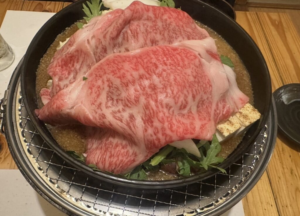 牛弁慶の牛鍋用「黒毛和牛サーロイン」。霜降りが美しい大判のサーロインが黒皿に盛り付けられている。