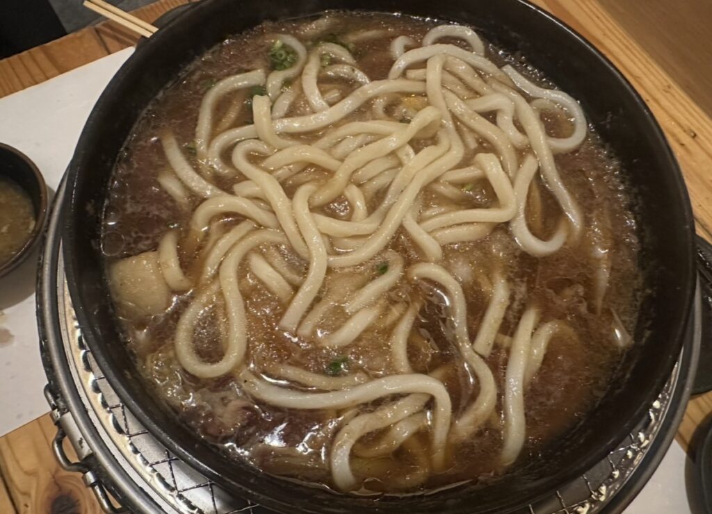 牛鍋の〆に提供された柚子おろしうどん。鍋のスープにもちもちのうどんがたっぷり入り、旨みが染み込んでいる様子。