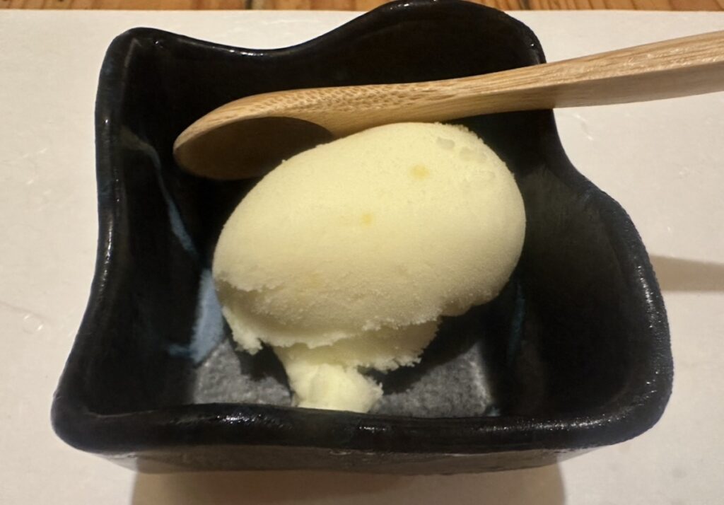 牛弁慶のデザート「本日の水菓子」。黒い器に盛られた柚子シャーベットと木製スプーンが添えられている。