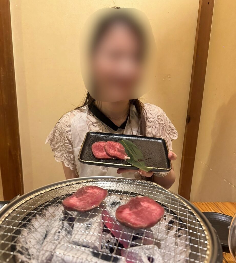 七輪で牛タンを焼きながら、皿を持って笑顔を見せるブログ運営者COCO。※顔はぼかしを入れて掲載しています。