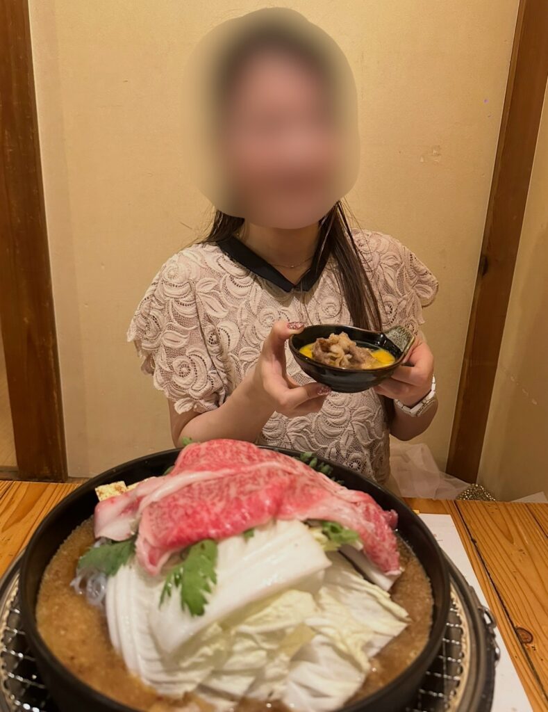 牛鍋のサーロインを手に笑顔を見せるブログ運営者COCO。大鍋に盛られた霜降り肉と野菜も写っている。※顔はぼかしを入れて掲載しています。