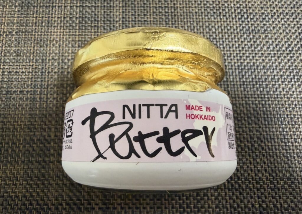 ニッタ（5186）の株主優待で毎年届く「牧田牧場の北海道バター」。白いガラス瓶にゴールドのフタが特徴で、香りとコクのある風味が魅力。