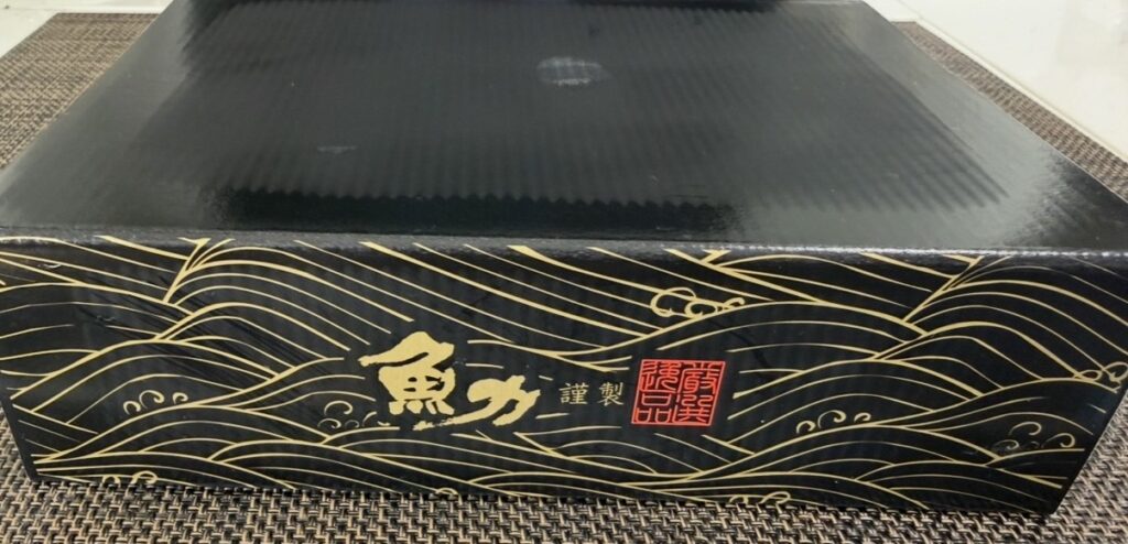 魚力の株主優待が入った黒×金デザインの専用ギフト箱。高級感のある箱が届いた様子の写真。
