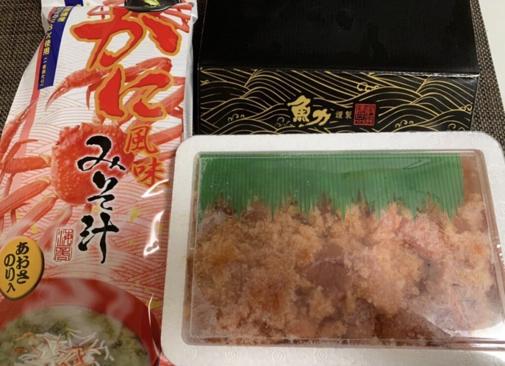 魚力の過去の記念株主優待として贈られた、かに風味みそ汁と無着色明太子が並んだセットの写真。黒いギフト箱入りで豪華感のある優待内容