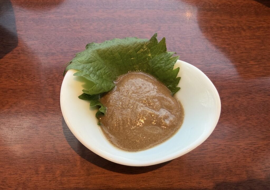 北の味紀行と地酒 北海道のコースで最初に提供された小鉢の蟹味噌。大葉が添えられた濃厚な蟹味噌の前菜。