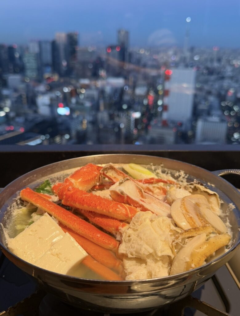 夜景を背景にしたカレッタ汐留店の蟹鍋。タラバ蟹とずわい蟹、帆立や豆腐が入った豪華な蟹鍋がグツグツ煮えている様子。