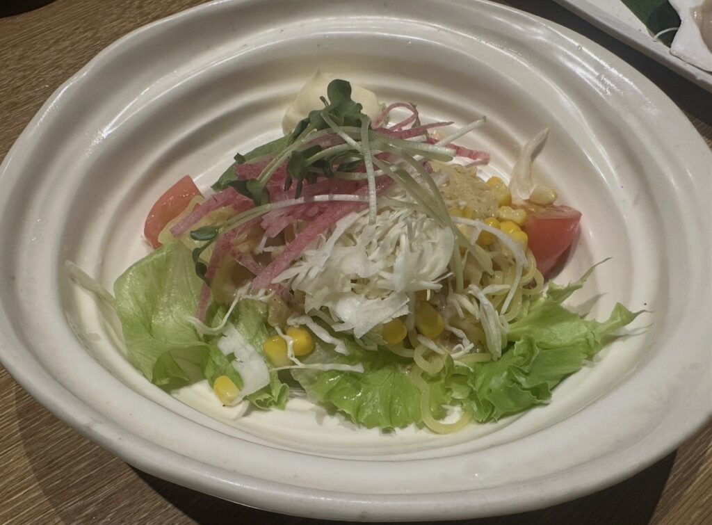 北海道名物ラーメンサラダ。中華麺の上にレタスやコーン、紅芯大根などが彩りよく盛り付けられている。