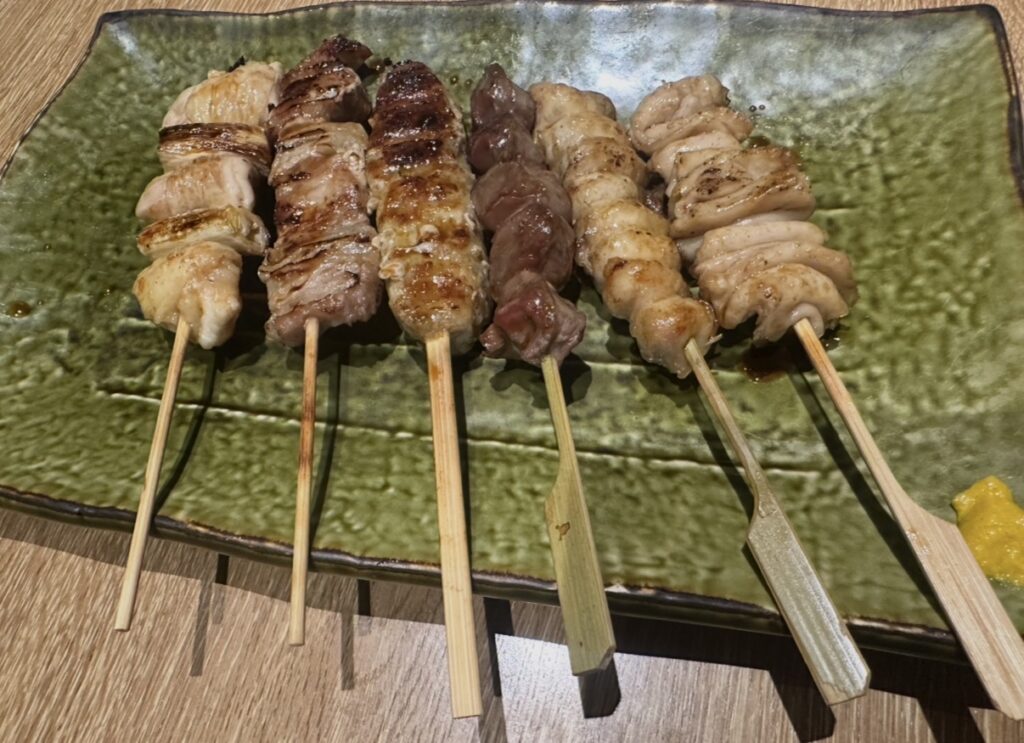 焼き鳥6本盛り合わせ。ねぎま、つくね、ハツ、皮などの定番串が並ぶ緑の和皿。