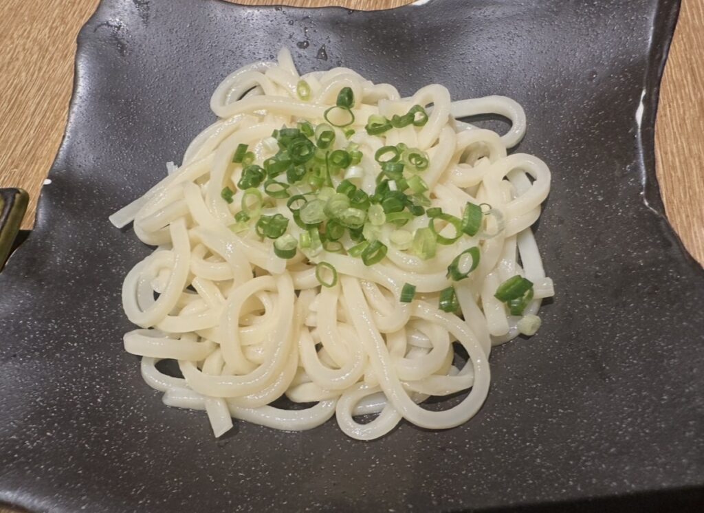 黒いお皿に盛りつけられたシンプルなしめのうどん。つやのある麺の上に刻みネギがたっぷりトッピングされており、つるんと喉越しの良さそうな一品。
