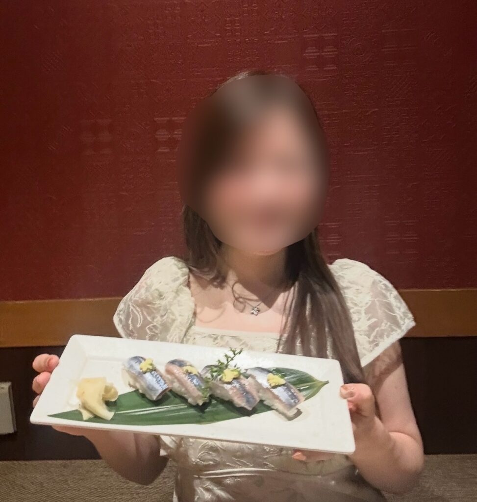 ブログ運営者COCOが旬の秋刀魚寿司を手に持って笑顔でポーズ。※顔はぼかしを入れて掲載しています。