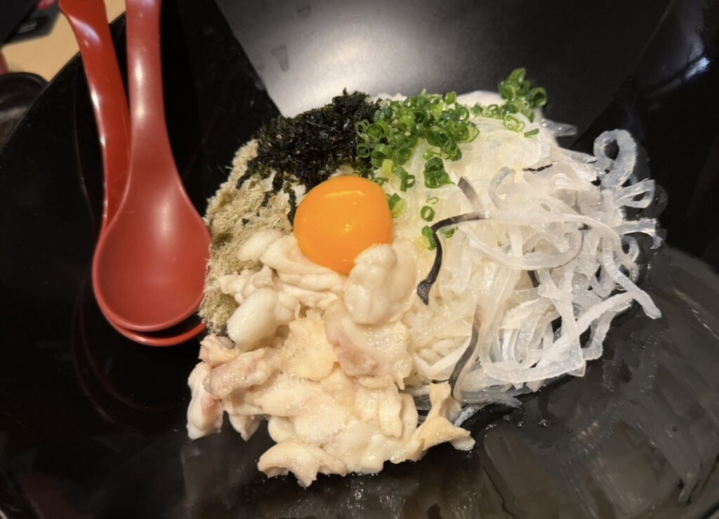 とらふぐ亭 目黒店の玄海コースで提供された名物ふぐ飯。ふぐの身と皮、ねぎ、海苔、とろろ昆布、卵黄がトッピングされ、混ぜて食べるスタイルの一品。
