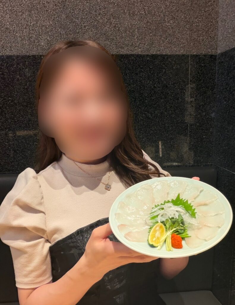 とらふぐ亭の泳ぎてっさを手に持ち、笑顔を浮かべるブログ運営者COCOの写真。お気に入りのふぐ刺しに満足した様子。※顔はぼかしを入れて掲載しています。