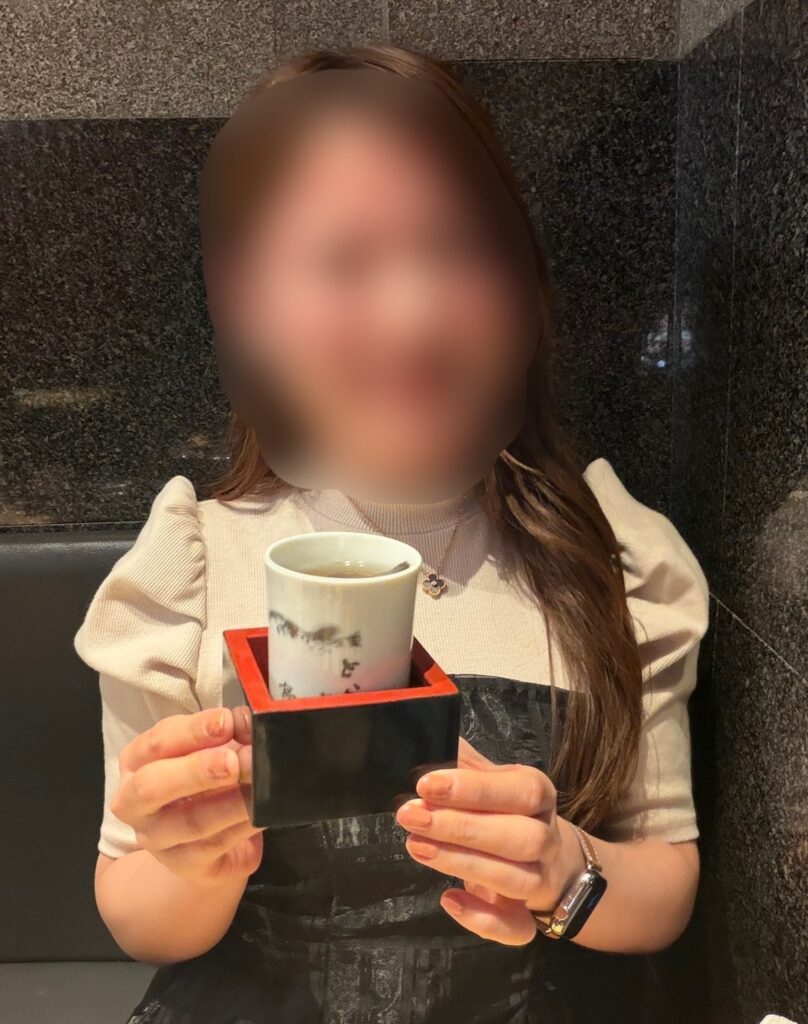 とらふぐ亭のひれ酒を手に持つブログ運営者COCOの写真。温かいひれ酒を楽しみながら、ふぐ料理の余韻に浸る様子。※顔はぼかしを入れて掲載しています。