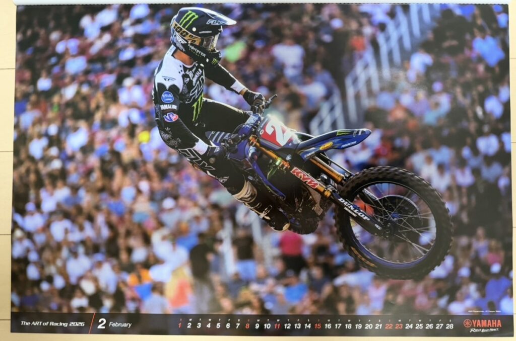 ヤマハ発動機のレーシングカレンダー2026年版・2月の写真。AMA Supercrossのソルトレイクシティラウンドで、クーパー・ウェッブ(Cooper Webb)がYZ450Fに乗りジャンプセクションを飛び越える瞬間が写されている。背景には大勢の観客が映り、スーパークロス特有のダイナミックな躍動感が伝わる一枚。