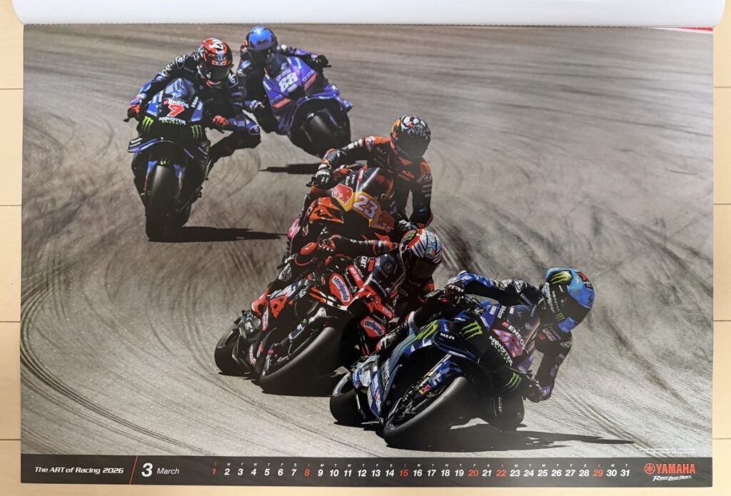 ヤマハ発動機のレーシングカレンダー2026年版・3月の写真。MotoGP World ChampionshipアラゴンGPで、アレックス・リンス(Álex Rins)とアウグスト・フェルナンデス(Augusto Fernández)、ミゲル・オリベイラ(Miguel Oliveira)らがYZR-M1に乗り、コーナーで激しいバトルを展開するシーンが写されている。路面には無数のタイヤ痕が残り、MotoGP特有のスピード感と緊張感が伝わる一枚。