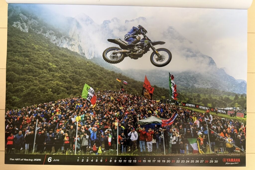 ヤマハ発動機のレーシングカレンダー2026年版・6月の写真。Motocross World Championship(MXGP)トレントINO大会で、マキシム・ルノー(Maxime Renaux)がYZ450FMに乗り、大観衆の頭上を大ジャンプする迫力あるシーンが写されている。背景には山々と霧が広がり、MXGP特有のスケールの大きさと臨場感が伝わる一枚。