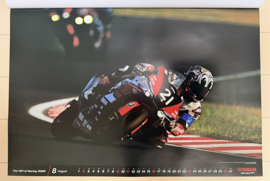 ヤマハ発動機のレーシングカレンダー2026年版・8月の写真。世界耐久選手権(EWC)・鈴鹿8耐で、中須賀克行(Katsuyuki Nakasuga)がYZF-R1を操り、ナイトセクションを鋭く攻める姿。ライトに照らされた路面と暗闇のコントラストが迫力を生み、耐久レース特有の緊張感とスピード感が伝わる一枚。