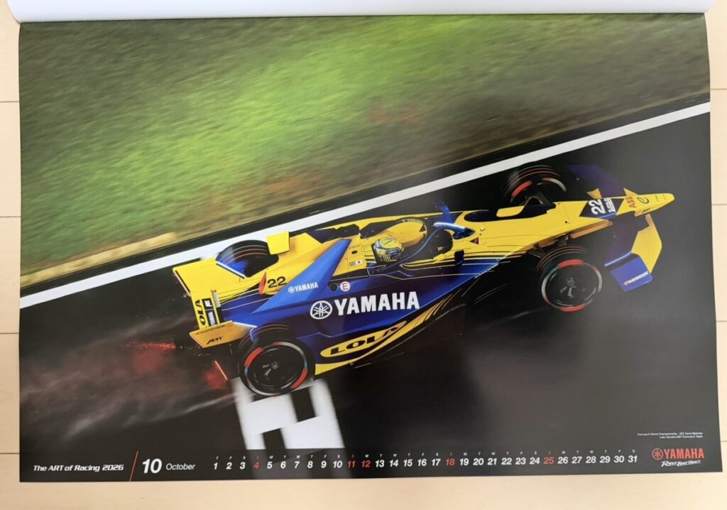 ヤマハ発動機のレーシングカレンダー2026年版・10月の写真。Formula E世界選手権の上海グランプリで、Zane Maloney(ゼイン・マロニー)が黄色と青のヤマハカラーをまとった Lola T001 を操り、濡れた路面を高速で走行する様子。後輪からスパークと水しぶきが上がり、フォーミュラEならではの迫力ある走りが表現された一枚。