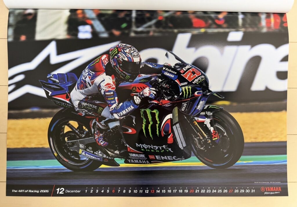 ヤマハ発動機のレーシングカレンダー2026年版・12月の写真。MotoGP世界選手権フランスGPで、ファビオ・クアルタラロ(Fabio Quartararo)がYZR-M1を深くバンクさせながら高速コーナーを攻めるシーン。ブラック×ブルーのモンスターエナジーカラーが映え、躍動感とスピード感あふれる一枚。