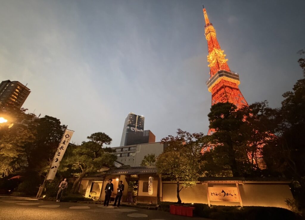 夕暮れの空にライトアップされた東京タワーと、歴史ある門構えが印象的な「とうふ屋うかい 芝店」の外観。温かい灯りがともる入口と庭木が、美しい和の雰囲気を演出している写真。