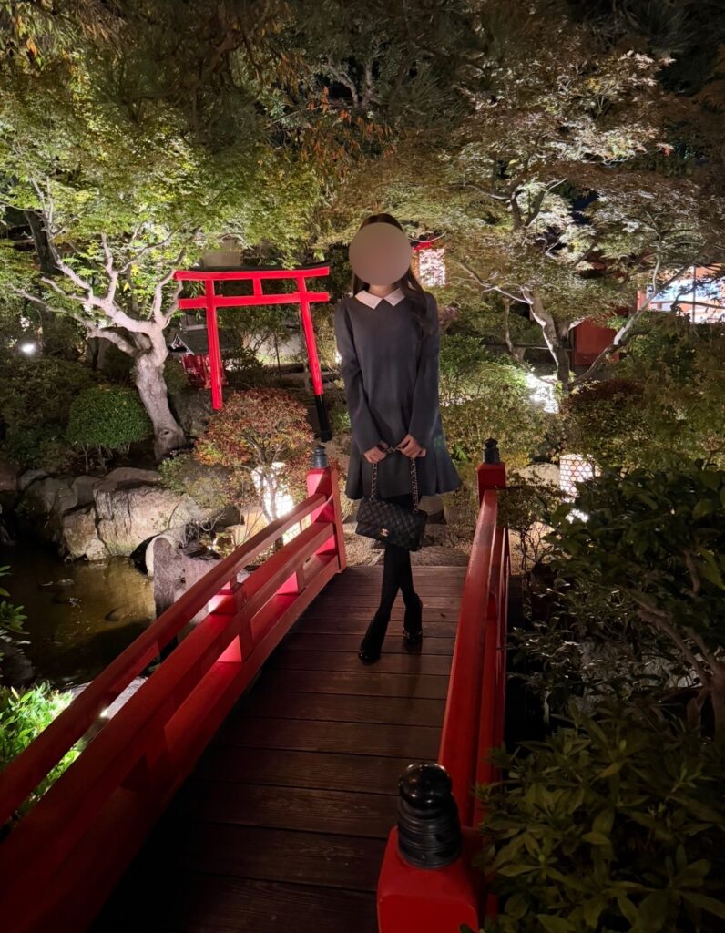 とうふ屋うかい芝店の庭園にある赤い橋の上で撮影したブログ運営者COCOの写真。背景には赤い鳥居とライトアップされた木々が広がり、静かな池の水面が光を映す幻想的な夜の雰囲気が伝わる一枚。※顔はぼかしを入れて掲載しています。