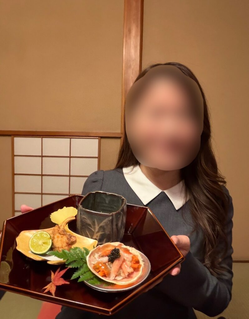 とうふ屋うかい芝店の特別会席「芝の八寸」を手にするブログ運営者COCO。香箱蟹やふぐの唐揚げなど、前菜が美しく盛り付けられた様子。※顔はぼかしを入れて掲載しています。